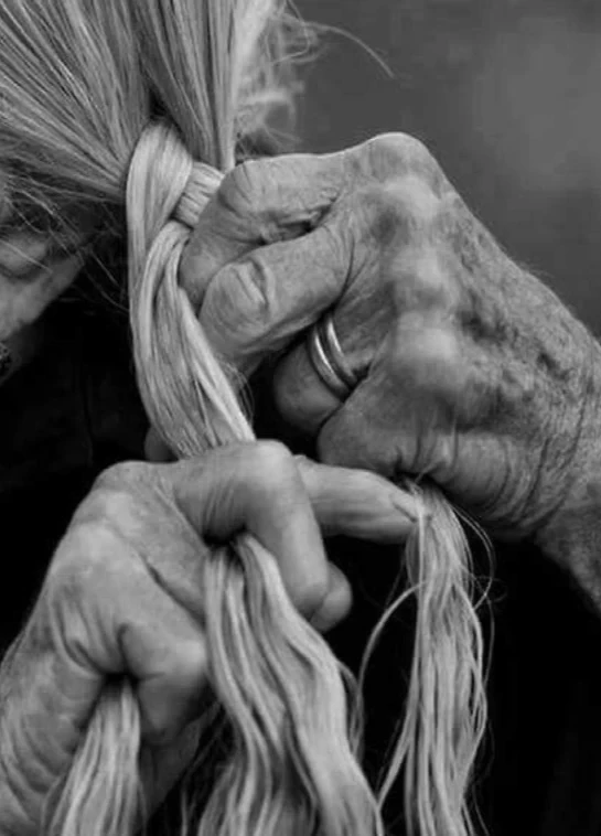 A caregiver's hands braiding an older person's long white hair.